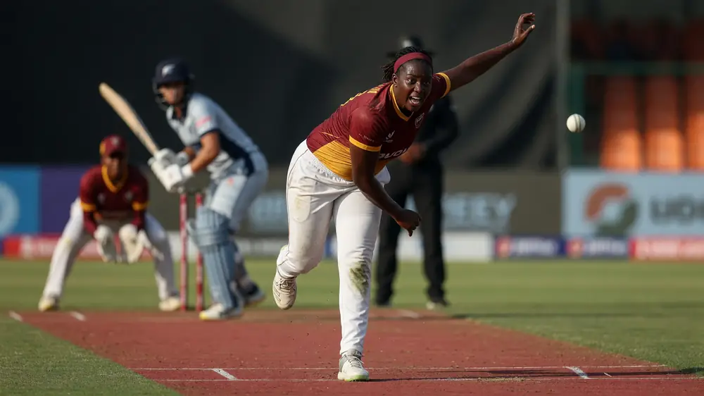 Female batter in whites drives through the off side during a professional T20 match, with the wicketkeeper and slip cordon blurred behind
